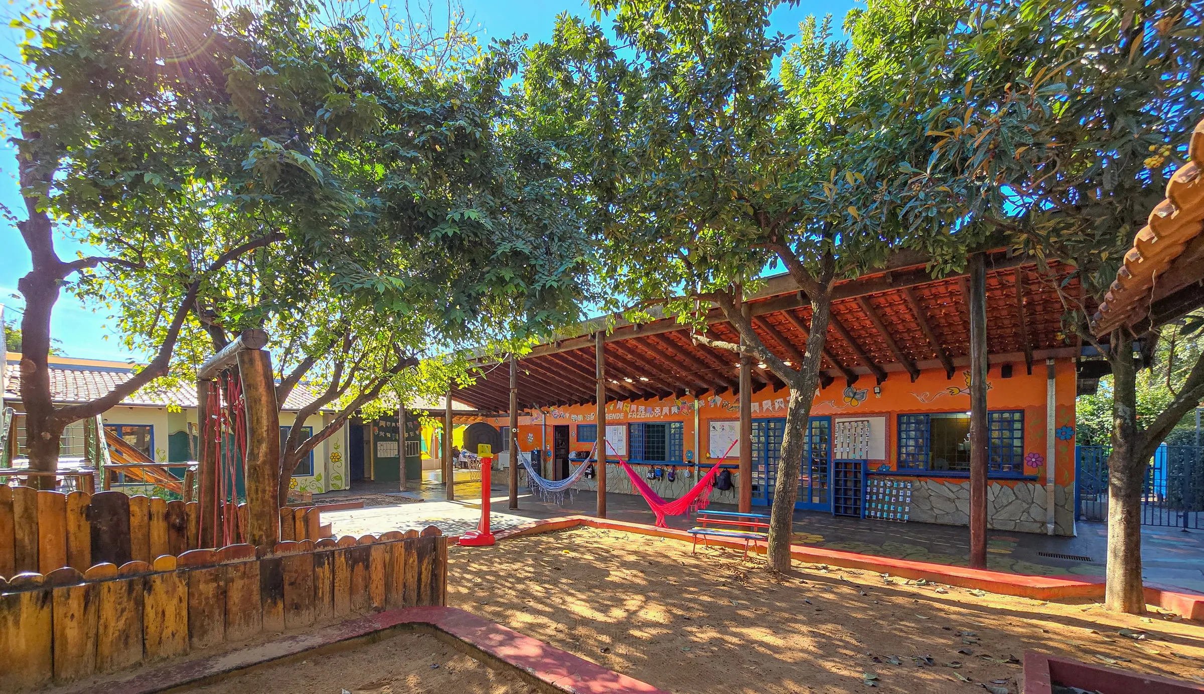Pátio arborizado da sede da Te Apoio, com redes e casa colorida