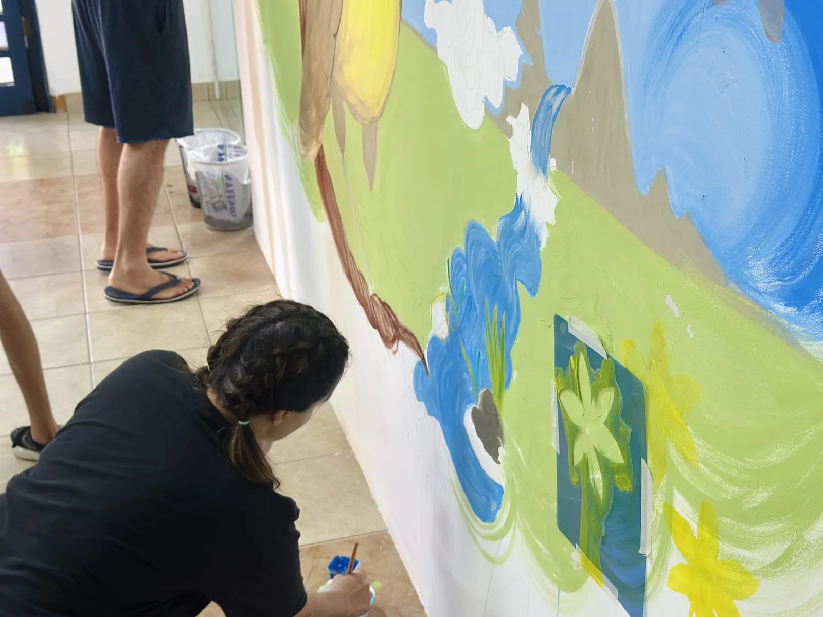 Participante pintando a parte de baixo do mural, agachada no chão