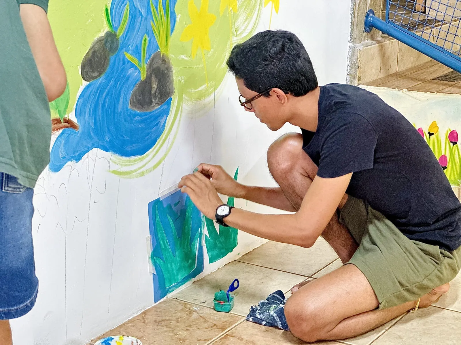Participante agachado pintando folhas verdes no mural