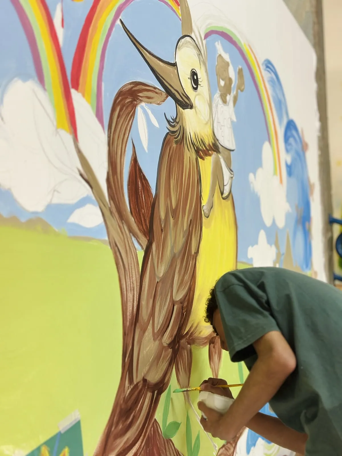 Detalhe do pássaro amarelo pintado no mural, com arco-íris e nuvens