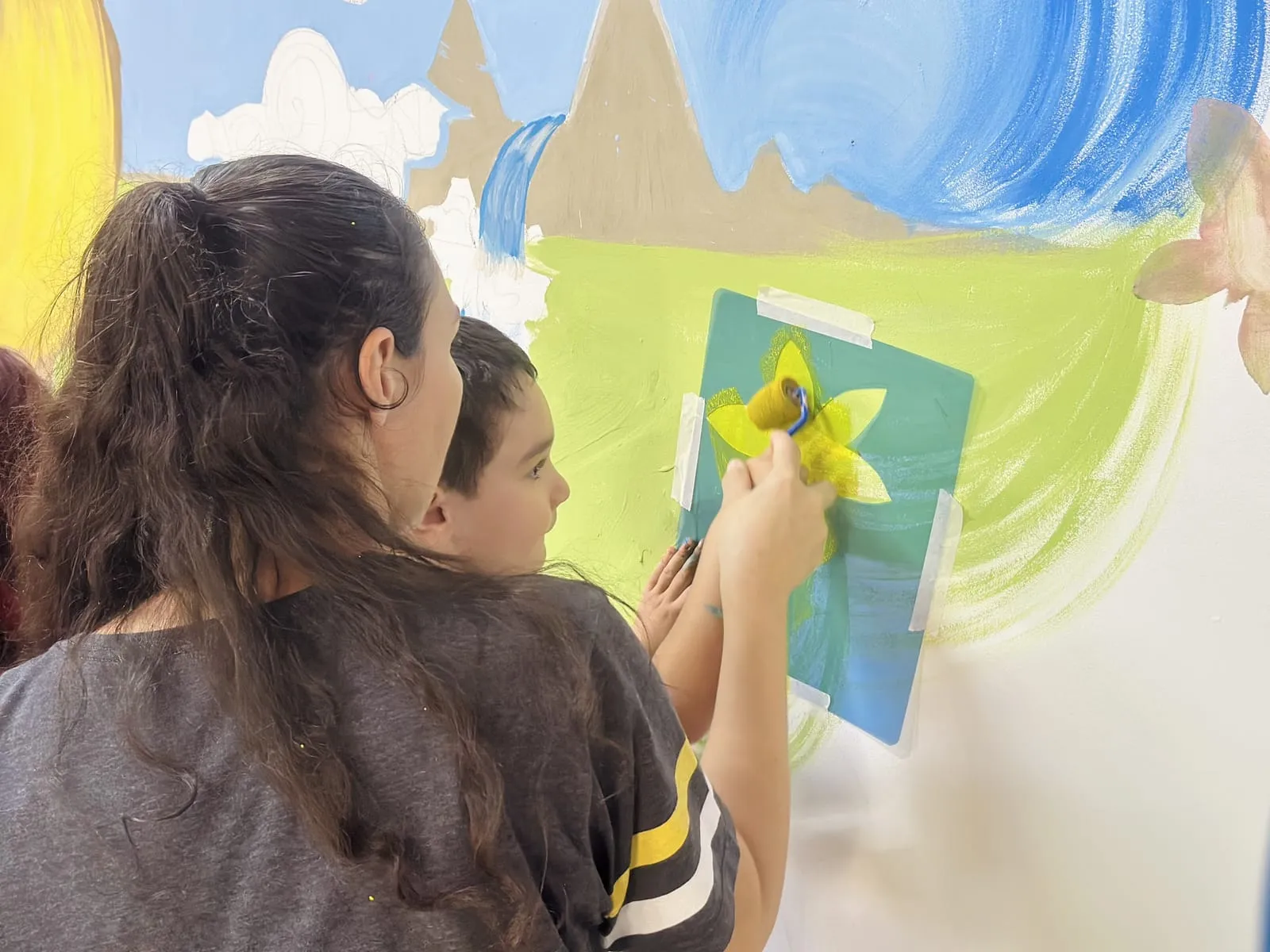Participante aplicando uma flor amarela com molde de estêncil no mural