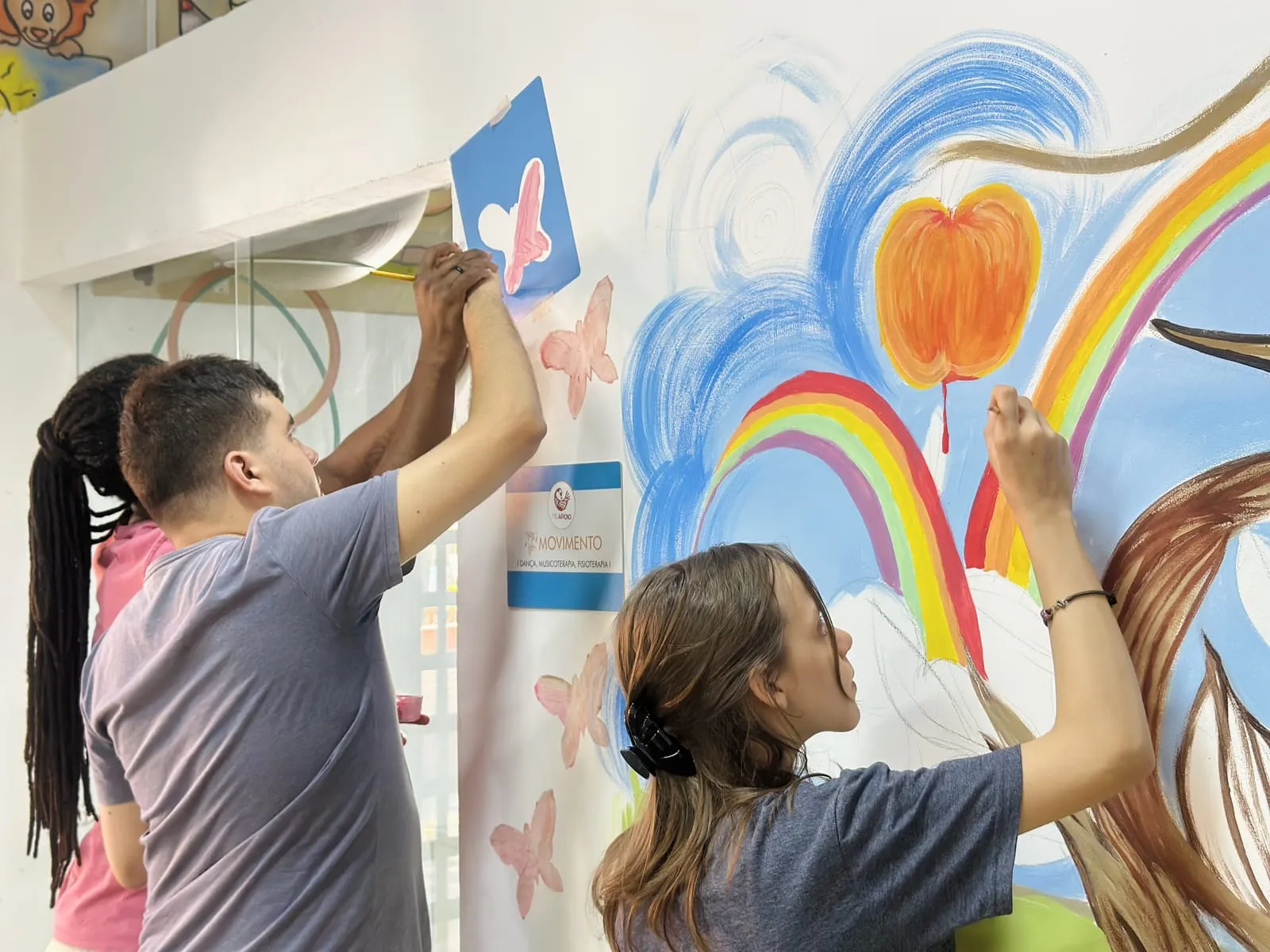 Participantes pintando borboletas e arco-íris na parede