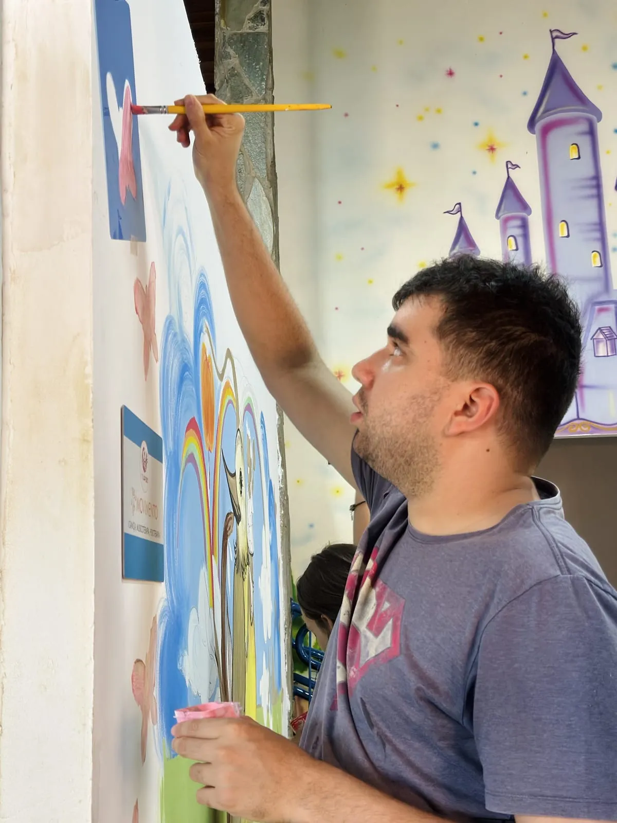 Participante pintando o mural ao lado de um castelo desenhado na parede