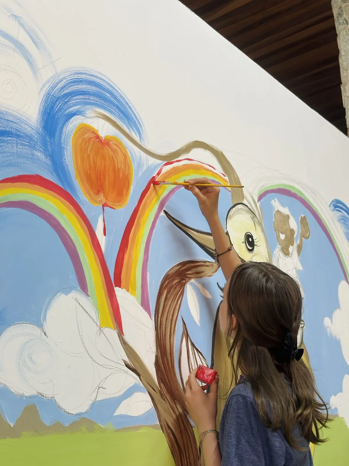 Menina pintando o arco-íris e o pássaro amarelo do mural