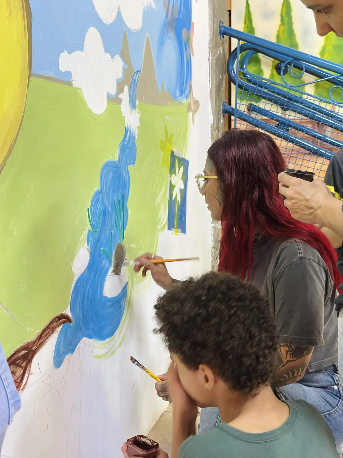Participantes pintando o céu e as nuvens do mural