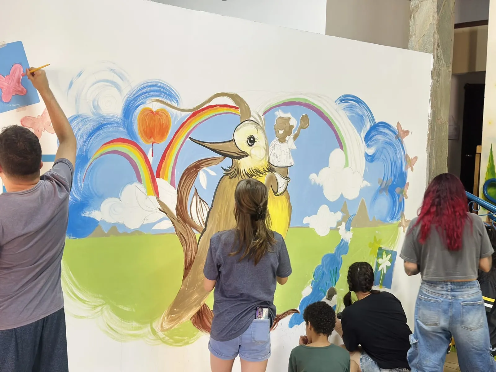 Grupo pintando o mural com o pássaro amarelo e o arco-íris
